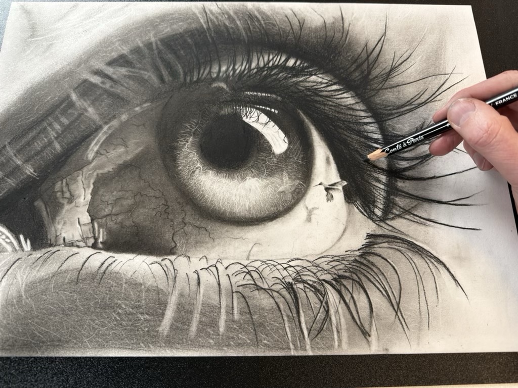 Een hand met een houtskoolpotlood werkt aan de tekening van het oog